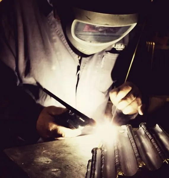 Saldatore con maschera protettiva durante una saldatura TIG su un pezzo metallico curvo