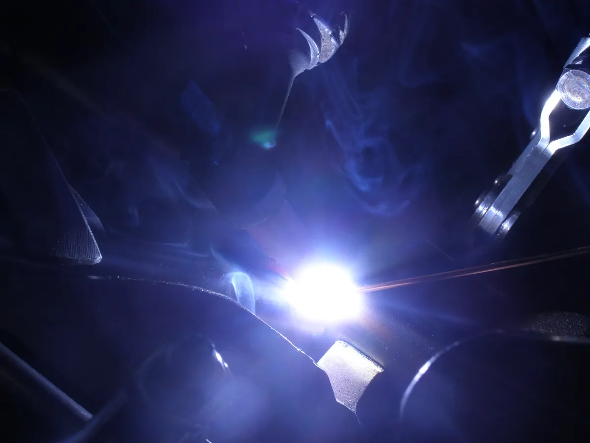 Primo piano dell'arco elettrico durante una saldatura TIG su un componente da corsa